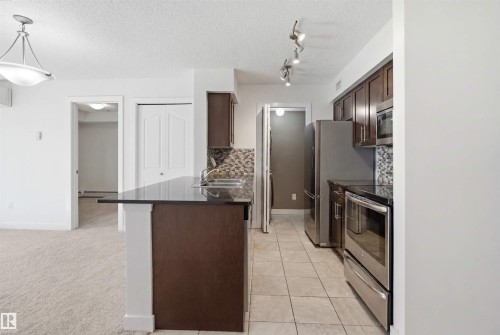 Kitchen featuring dark wood-finish cabinetry, stainless steel appliances, and a tiled backsplash - 115 274 Mcconachie Drive, Edmonton, AB 
