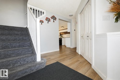 Entryway featuring wood-finish flooring, white trim, and a carpeted staircase with white railing - 8523 7 Avenue Sw, Edmonton, AB 