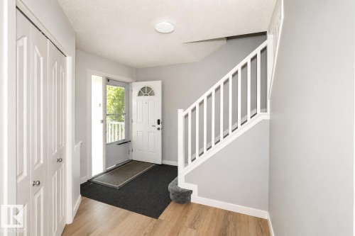 Entryway featuring wood-finish flooring, a white staircase with carpeted treads, and a front door with an arched glass insert - 8523 7 Avenue Sw, Edmonton, AB 