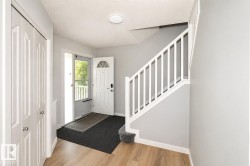Entryway featuring wood-finish flooring, a white staircase with carpeted treads, and a front door with an arched glass insert - 