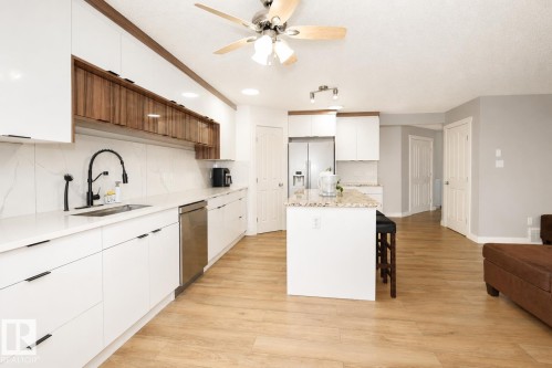 Modern kitchen featuring a central island with a granite-style countertop, integrated stainless steel appliances, and wood-finish flooring - 8523 7 Avenue Sw, Edmonton, AB 