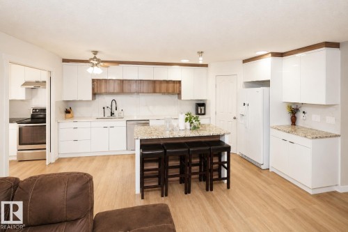 Kitchen featuring white cabinetry, light wood-finish flooring, and a central island with a granite-style countertop - 8523 7 Avenue Sw, Edmonton, AB 