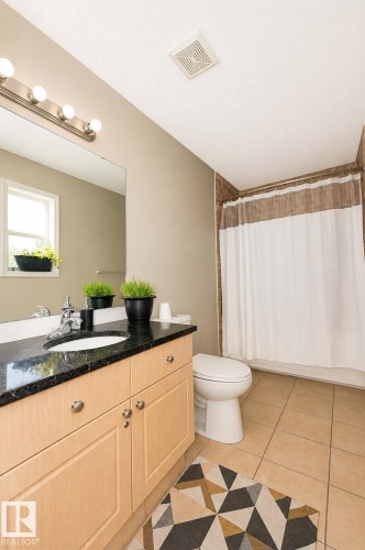 Bathroom featuring a light wood-finish vanity with an undermount sink, dark granite countertop, and brushed nickel hardware - 8523 7 Avenue Sw, Edmonton, AB 