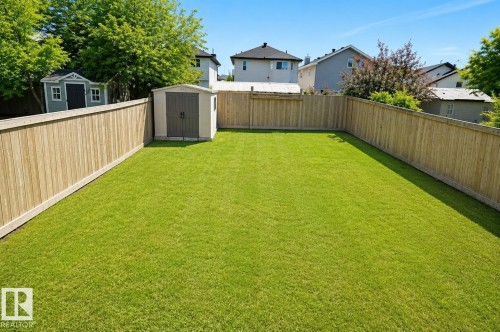 Spacious backyard featuring an expanse of green lawn, full wood fencing, and a permanent storage shed - 8523 7 Avenue Sw, Edmonton, AB 