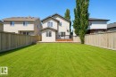 Spacious backyard featuring a large green lawn, perimeter wood fencing, and a multi-level wood deck with black metal railings - 8523 7 Avenue Sw, Edmonton, AB 