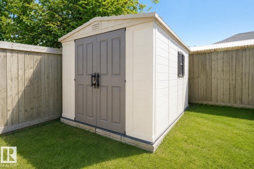 Detached storage shed with double doors, wood-finish privacy fencing, and a manicured lawn - 8523 7 Avenue Sw, Edmonton, AB 