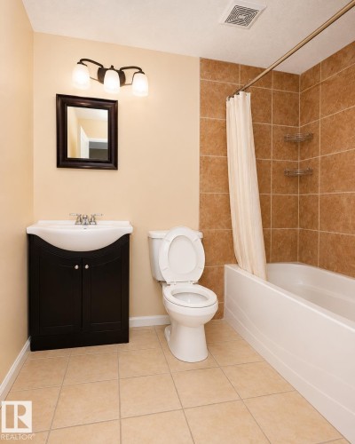Full bathroom featuring a dark wood-finish vanity with an integrated white sink, a vanity mirror, and a three-bulb sconce - 8523 7 Avenue Sw, Edmonton, AB 