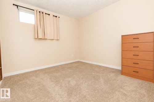 Room featuring neutral-toned walls, recessed window with a black rod, light-toned carpet, and white baseboards - 8523 7 Avenue Sw, Edmonton, AB 