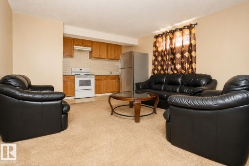 Open-concept living area featuring a kitchen with wood cabinetry, white appliances, and a tile backsplash - 8523 7 Avenue Sw, Edmonton, AB 