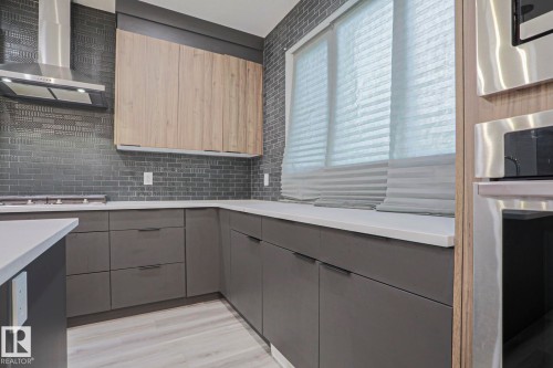 Modern kitchen featuring wood-finish flooring, dark gray cabinetry, light countertops, and a full tile backsplash - 10628 81 Street Nw, Edmonton, AB 