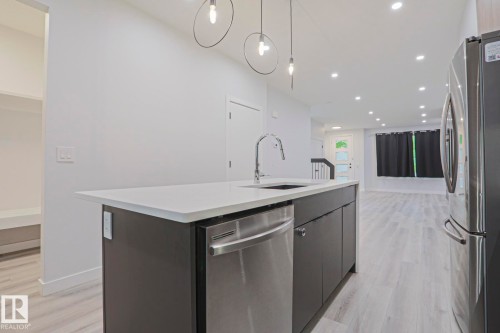 Kitchen island featuring a white countertop, undermount sink with a gooseneck faucet, and integrated stainless steel dishwasher - 10628 81 Street Nw, Edmonton, AB 