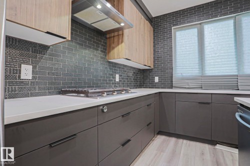 Contemporary kitchen featuring a built-in gas range, wood-finish upper cabinetry, and sleek dark gray lower cabinetry - 10628 81 Street Nw, Edmonton, AB 