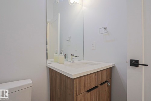 Bathroom featuring a wood-finish vanity with integrated sink, a light countertop, and a modern mirror - 10628 81 Street Nw, Edmonton, AB 