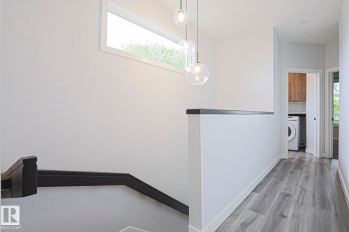Upper-level landing featuring wood-finish flooring, a contemporary pendant light fixture, and a horizontal window - 10628 81 Street Nw, Edmonton, AB 