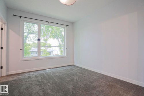 Light-filled room featuring a large white-framed window, neutral gray carpet, and white baseboards - 10628 81 Street Nw, Edmonton, AB 