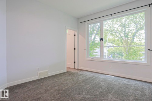 Room featuring a large window with black hardware, neutral wall paint, white trim, and gray carpet flooring - 10628 81 Street Nw, Edmonton, AB 