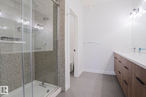 Modern bathroom featuring a glass-enclosed shower with speckled stone-finish walls, a rainfall showerhead, and a separate handheld shower - 10628 81 Street Nw, Edmonton, AB 