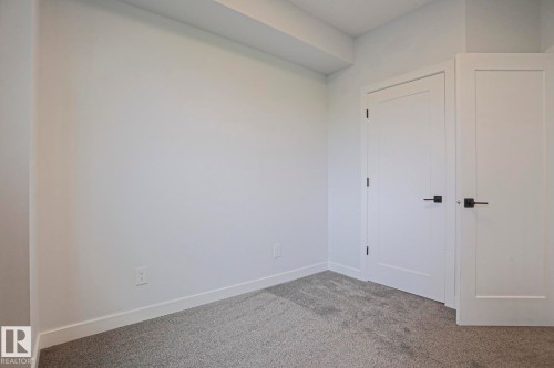 Carpeted room featuring white walls, white baseboards, two white interior doors, and matte black door hardware - 10628 81 Street Nw, Edmonton, AB 