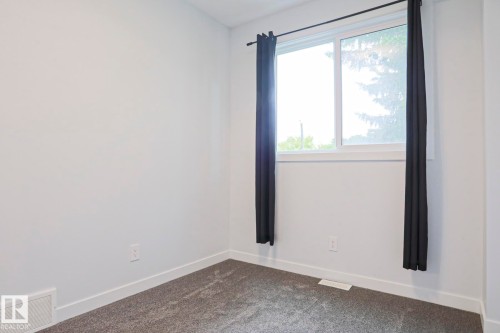Bright room featuring a large window, neutral wall paint, white trim, and gray carpet flooring - 10628 81 Street Nw, Edmonton, AB 