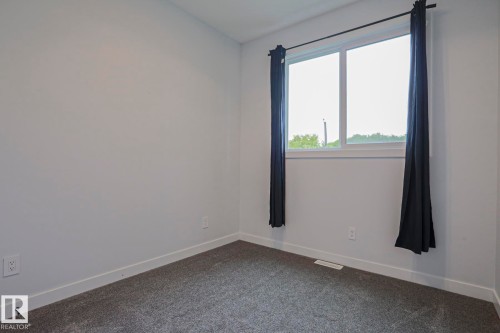Room featuring a double window with dark drapery rods and panels, light gray walls, dark gray carpet, and white baseboards - 10628 81 Street Nw, Edmonton, AB 
