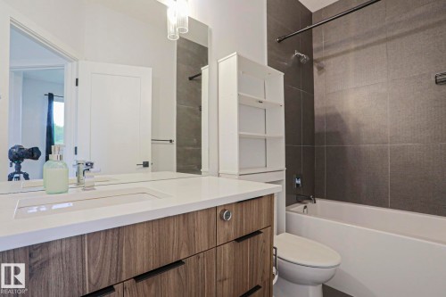 Bathroom featuring a wood-finish vanity with integrated sink, white countertop, and contemporary faucet - 10628 81 Street Nw, Edmonton, AB 