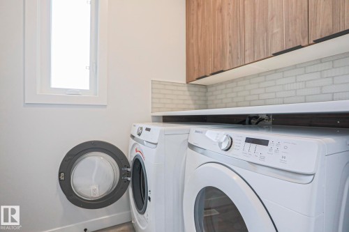 Functional laundry area featuring white appliances, a light wood-finish upper cabinet, a white subway tile backsplash, and a white countertop - 10628 81 Street Nw, Edmonton, AB 
