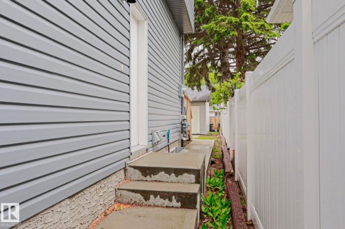 Exterior side entry with concrete steps and landing, gray horizontal siding, and a white privacy fence - 10628 81 Street Nw, Edmonton, AB 