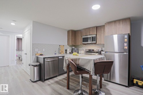 Contemporary kitchen featuring stainless steel appliances, light wood-finish cabinetry, a white subway tile backsplash, and light wood-finish flooring - 10628 81 Street Nw, Edmonton, AB 
