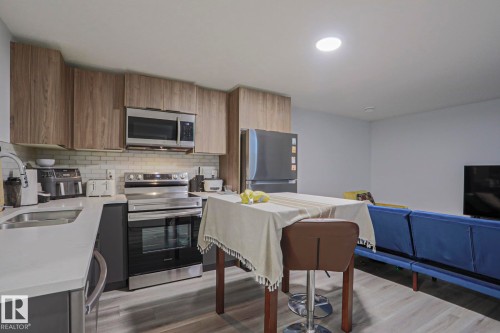 Modern kitchen featuring wood-finish upper cabinetry, stainless steel appliances, white subway tile backsplash, and light-toned countertops - 10628 81 Street Nw, Edmonton, AB 