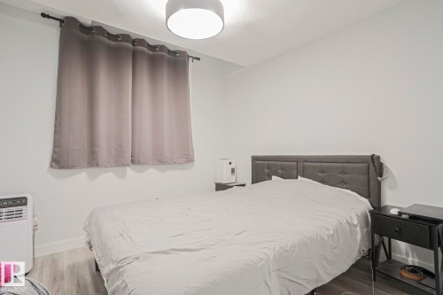 Room featuring light wood-finish flooring, white walls, a window with dark curtains, and an overhead light fixture - 10628 81 Street Nw, Edmonton, AB 