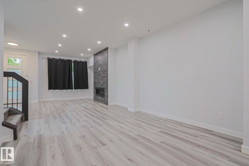 Spacious interior featuring light wood-finish flooring, recessed lighting, and a modern fireplace with a stacked stone facade - 10628 81 Street Nw, Edmonton, AB 