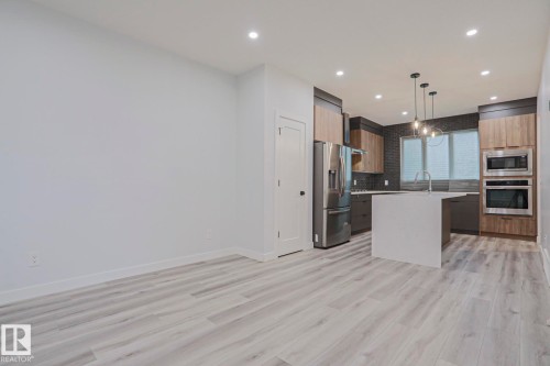 Open-concept kitchen featuring a large island with a waterfall countertop, stainless steel appliances, and wood-finish cabinetry - 10628 81 Street Nw, Edmonton, AB 