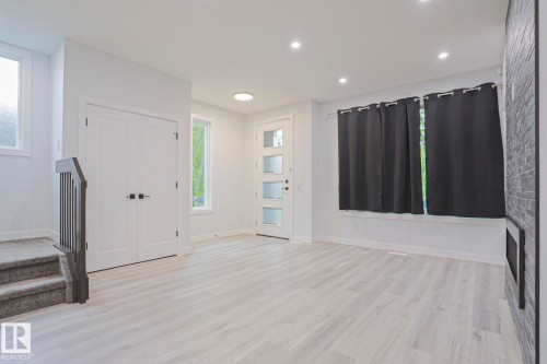 Bright, open living space featuring light wood-finish flooring, recessed lighting, and a modern entryway door with frosted glass panels - 10628 81 Street Nw, Edmonton, AB 