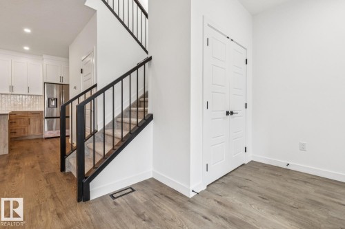 Open-concept layout with wood-finish flooring, a contemporary staircase with black metal balusters, and a kitchen featuring two-tone cabinetry - 11336 130 Street Nw, Edmonton, AB 