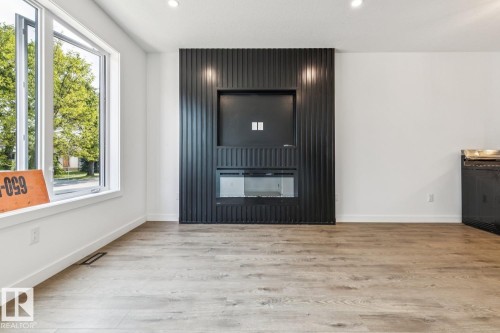 Contemporary electric fireplace with a fluted panel surround, wood-finish flooring, recessed lighting, and a casement window - 11336 130 Street Nw, Edmonton, AB 