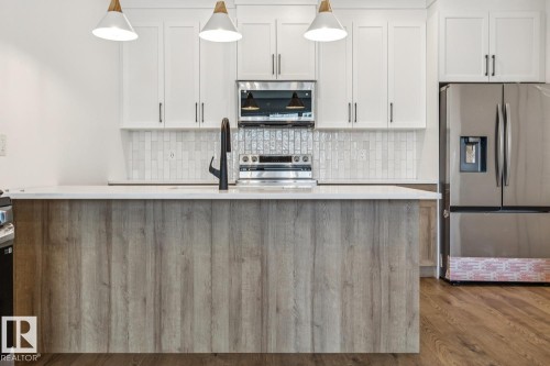 Kitchen featuring white cabinetry, a central island with wood-finish paneling, white countertop, vertical subway tile backsplash, and stainless steel appliances - 11336 130 Street Nw, Edmonton, AB 