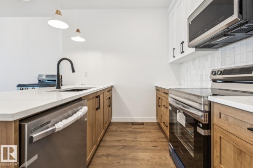 White countertops, wood-finish flooring, two-tone cabinetry, stainless steel appliances, and a tile backsplash - 11336 130 Street Nw, Edmonton, AB 
