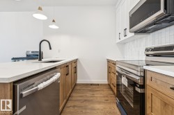 White countertops, wood-finish flooring, two-tone cabinetry, stainless steel appliances, and a tile backsplash - 