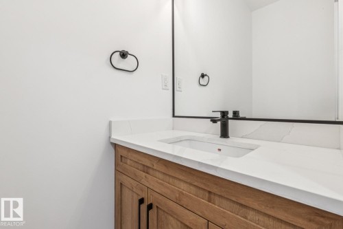 Wood-finish vanity with matte black hardware, white countertop with integral sink, matte black single-handle faucet, and framed wall mirror - 11336 130 Street Nw, Edmonton, AB 