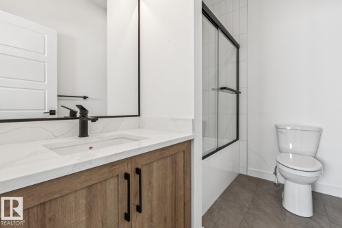 Wood-finish vanity with black hardware, white rectangular under-mount sink, white countertop with veining, and black-framed sliding glass shower enclosure - 11336 130 Street Nw, Edmonton, AB 