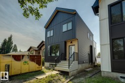 Modern exterior featuring corrugated black siding, an attached concrete staircase with black railings, and a light brick entrance - 