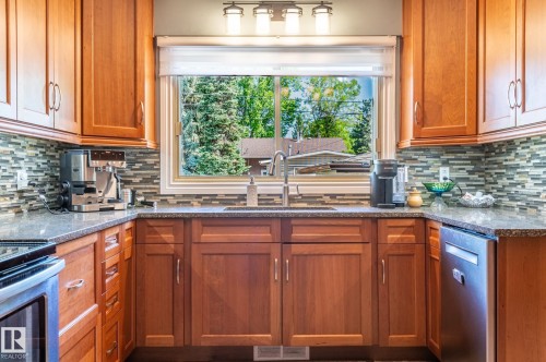 Kitchen featuring a large window, wood cabinetry, granite countertops, and a mosaic tile backsplash - 14708 108 Av, Edmonton, AB 