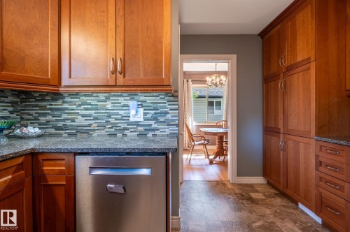 Kitchen featuring wood cabinetry, stainless steel dishwasher, granite-style countertops, and mosaic tile backsplash - 14708 108 Av, Edmonton, AB 