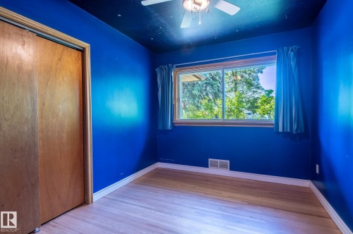 Bright interior space featuring a window with exterior tree views, light wood-finish flooring, a ceiling fan, baseboard trim, and a built-in closet with wood doors - 14708 108 Av, Edmonton, AB 