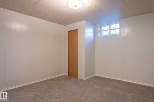 Carpeted room featuring white paneling, a wood-finish door, and a white-framed window - 14708 108 Av, Edmonton, AB 