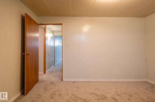 Carpeted room featuring light-toned paneling, white baseboards, and a wood-finish interior door - 14708 108 Av, Edmonton, AB 