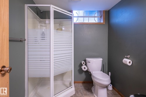 Compact bathroom featuring a corner shower with frosted and clear glass enclosure, a white commode, and textured gray wall paint - 14708 108 Av, Edmonton, AB 