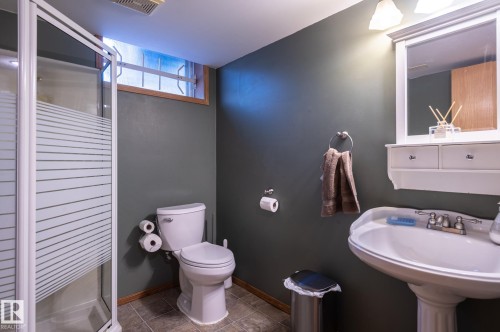 Bathroom featuring a pedestal sink, white framed mirror with wall-mounted lighting, a frosted glass shower enclosure with white framing, and dark wall paint - 14708 108 Av, Edmonton, AB 