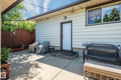 Concrete patio with an exterior entrance, white siding, and a privacy fence - 14708 108 Av, Edmonton, AB 