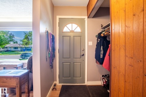 Entryway featuring a paneled door with a half-moon glass insert, wood-finish flooring, and a built-in closet with sliding wood panel doors - 14708 108 Av, Edmonton, AB 